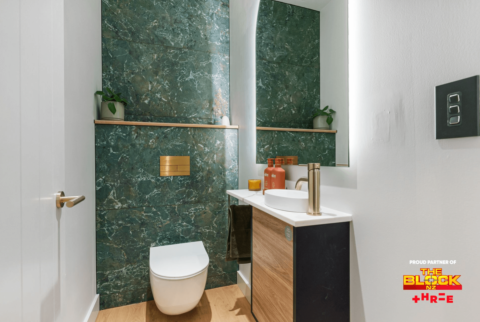 Compact powder room with green marble feature wall, wall-hung toilet, timber vanity, and gold fixtures
