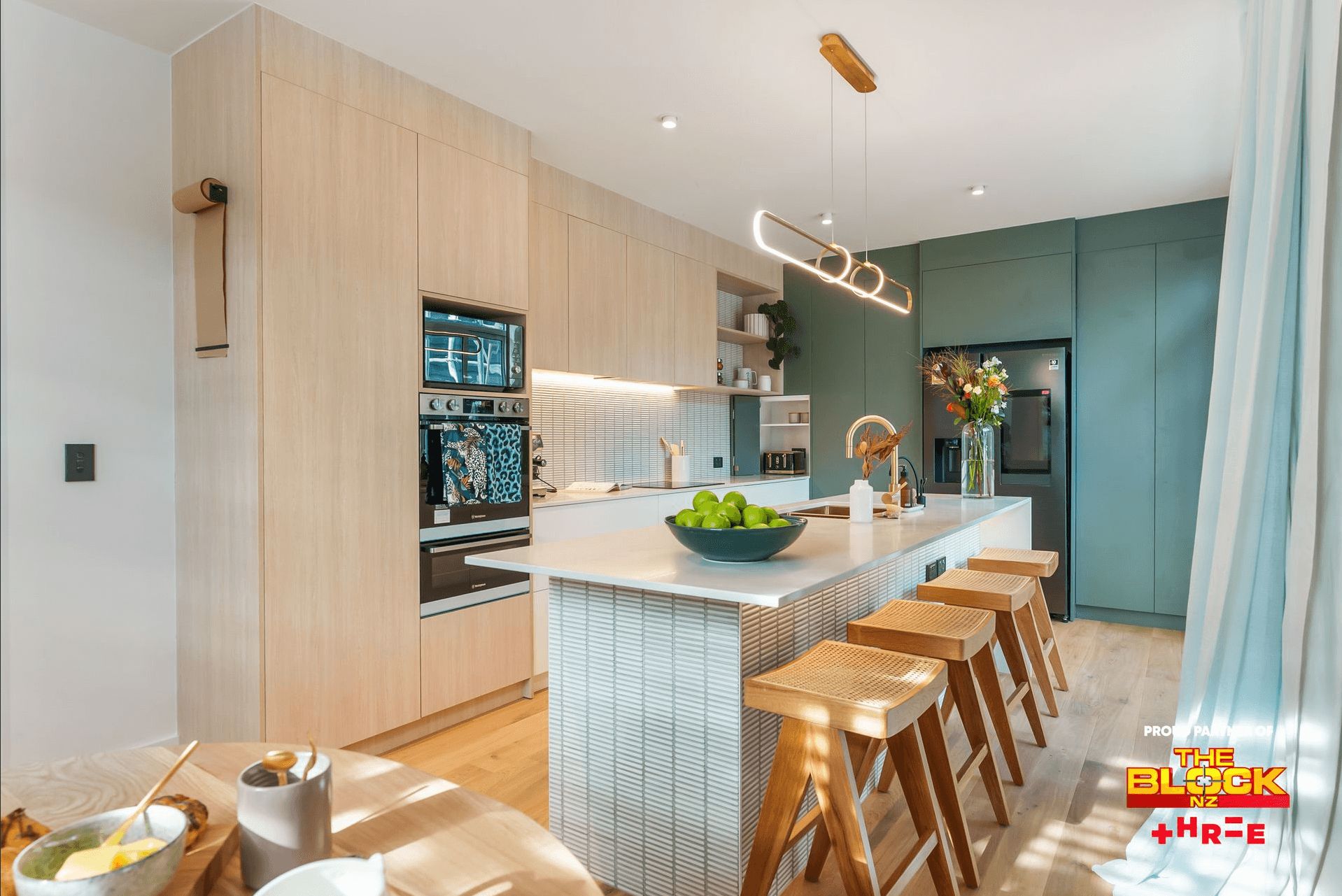 Modern kitchen with light wood cabinetry, sage green accent cabinets, white countertops, and wooden bar stools