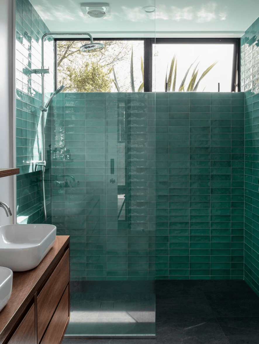 Contemporary bathroom with teal subway tiles, white vanity with wood accents, gold fixtures, and glass shower enclosure