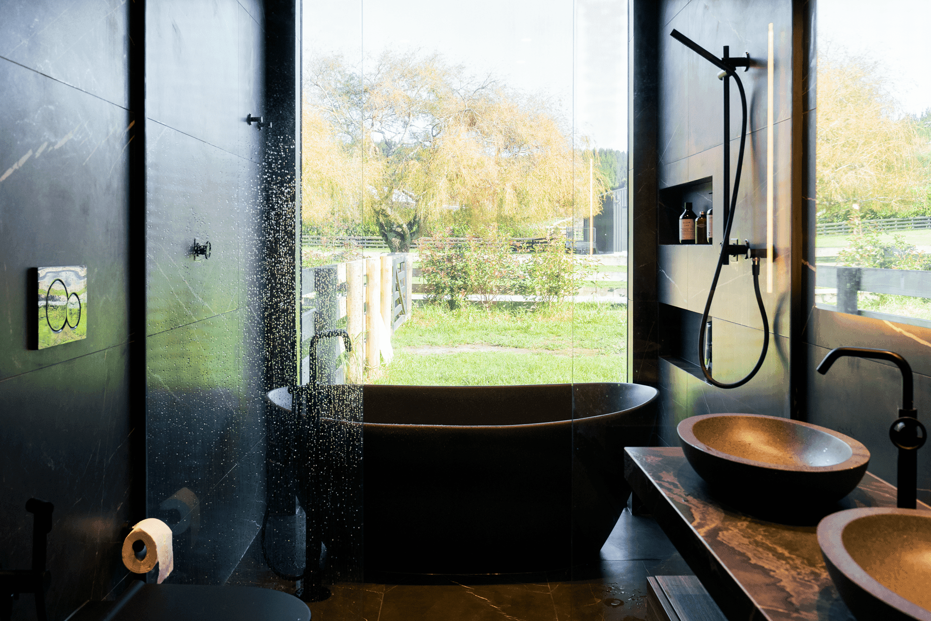 Modern luxury bathroom with black tiled walls, freestanding bathtub, and panoramic window view