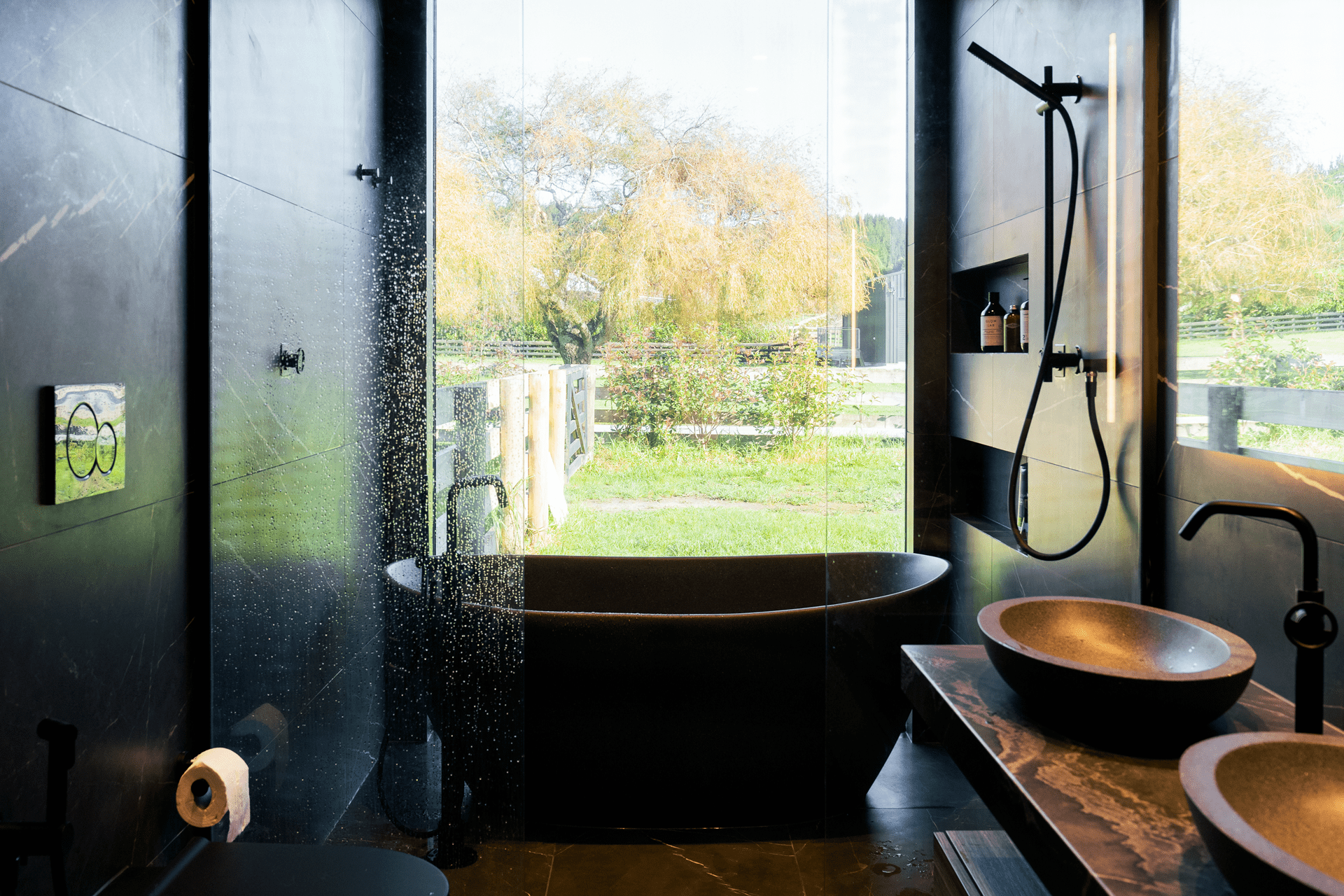 Modern luxury bathroom with black tiled walls, freestanding bathtub, and panoramic window view
