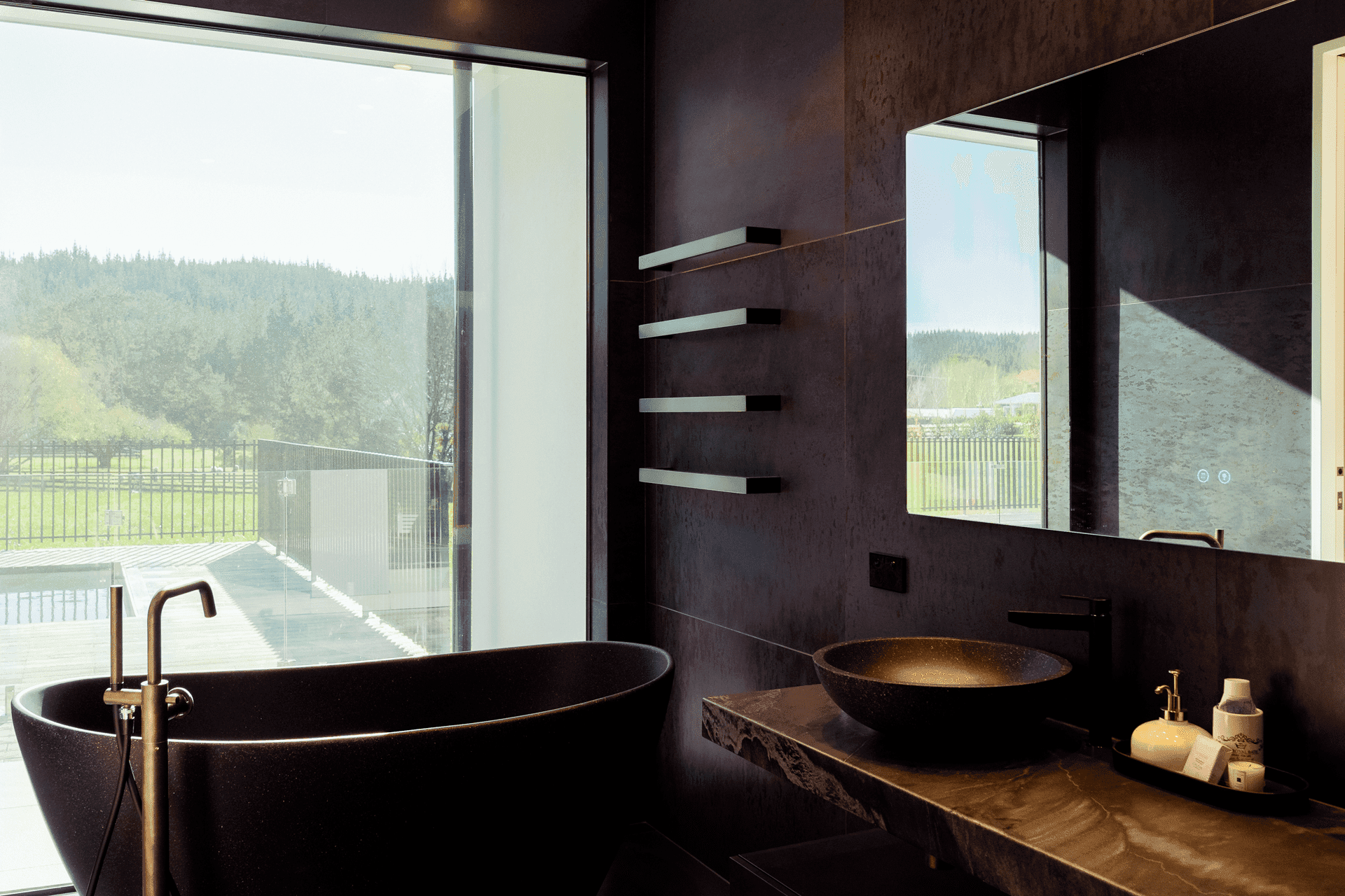 Dramatic bathroom with black marble, black freestanding tub, dual vessel sinks, brushed gold fixtures, and countryside views