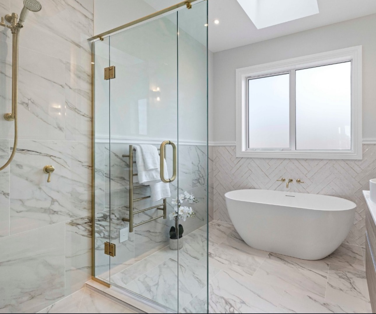 Luxury bathroom with marble tiling, glass shower enclosure with gold fixtures, and freestanding bathtub