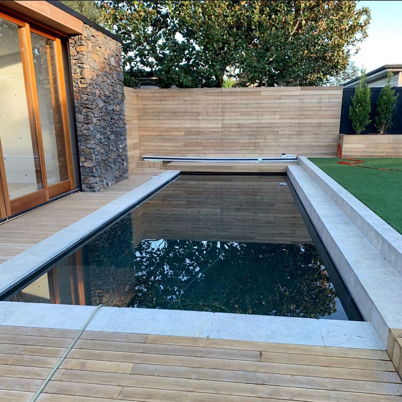 Modern outdoor pool with elegant stone coping and wooden decking, showcasing premium tiling craftsmanship
